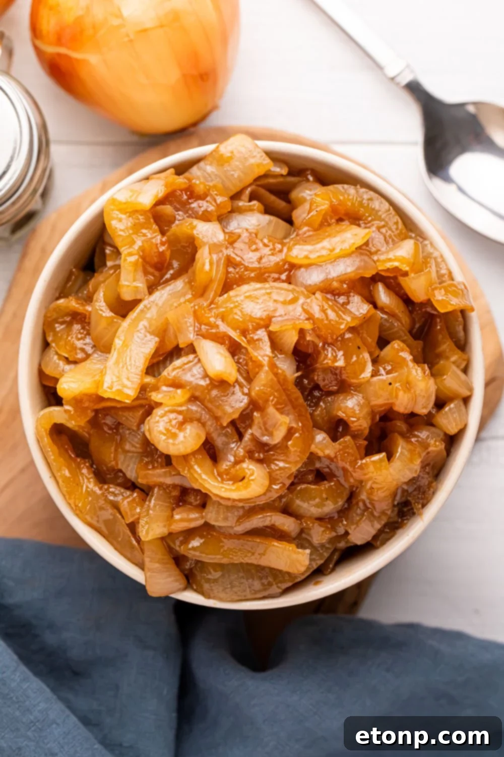CrockPot Caramelized Onions in a bowl with an onion and a spoon to the side of spoon on table 