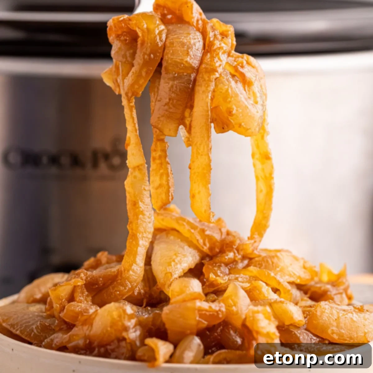 CrockPot Caramelized Onions in a bowl with the CrockPot behind it on table
