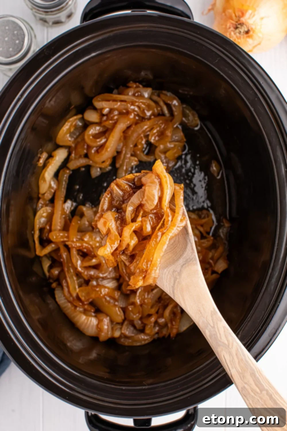 Crockpot with Caramelized onions in it with a wooden spoon stirring some of the onions around 