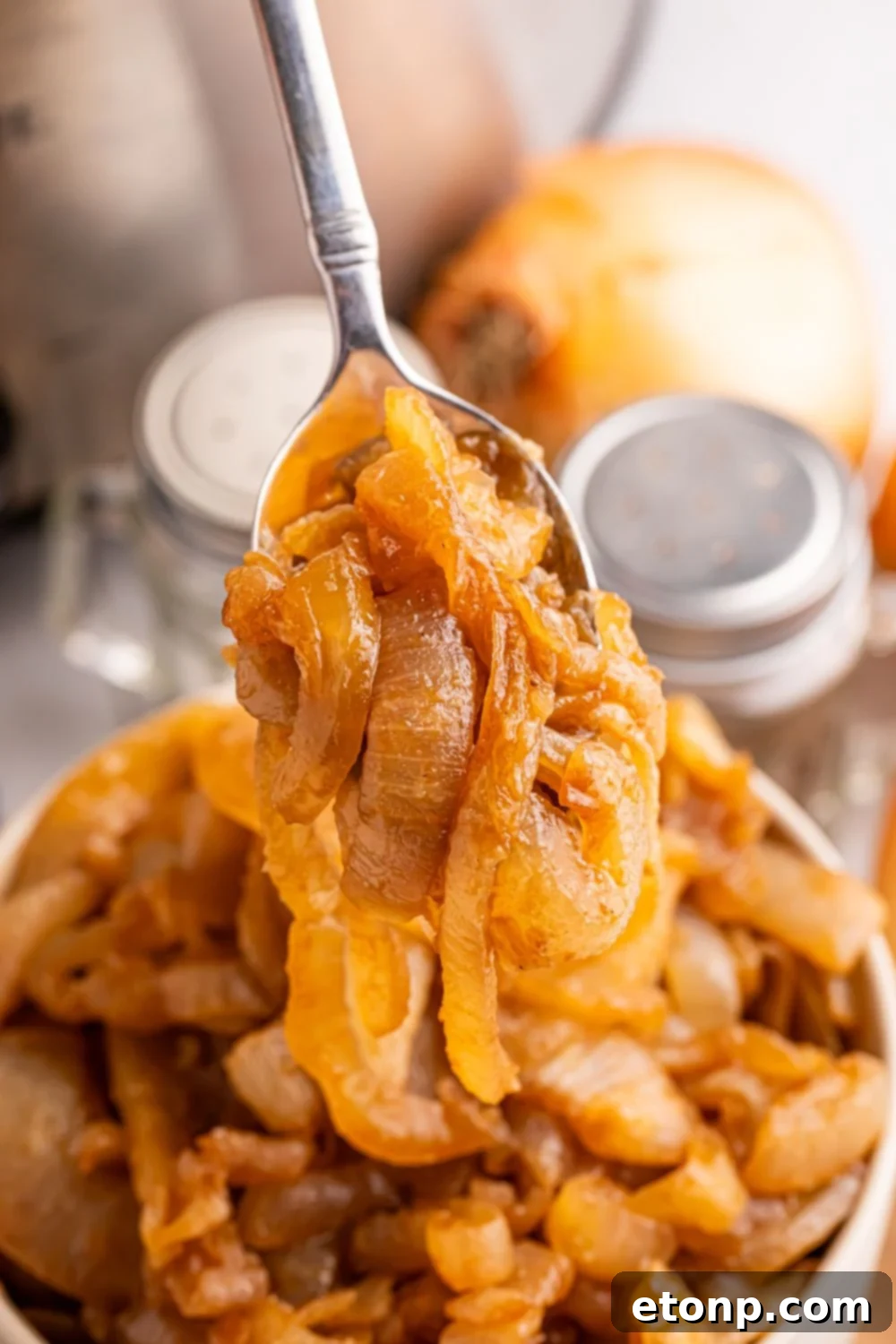 spoon scooping up some of the CrockPot Caramelized Onions out of a bowl on table. Salt and pepper shakers to the side of bowl on table 