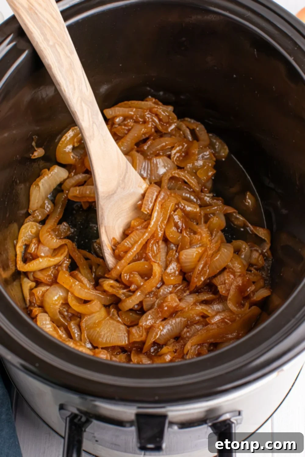 overhead look of CrockPot caramelized onions with a wooden spoon in container