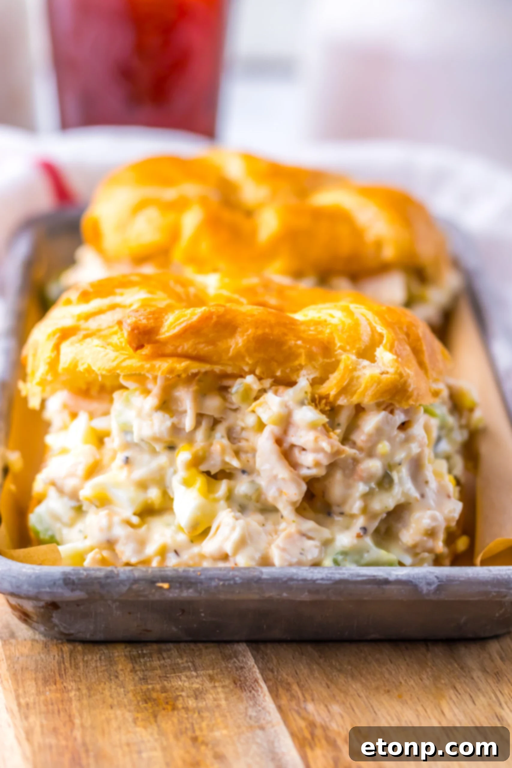 Close up shot of chicken salad on a white croissant on a tin tray.  