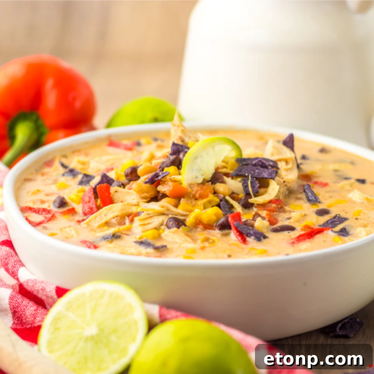 Close up side view of a bowl of tortilla soup topped with tortilla chips, corn, and beans. 
