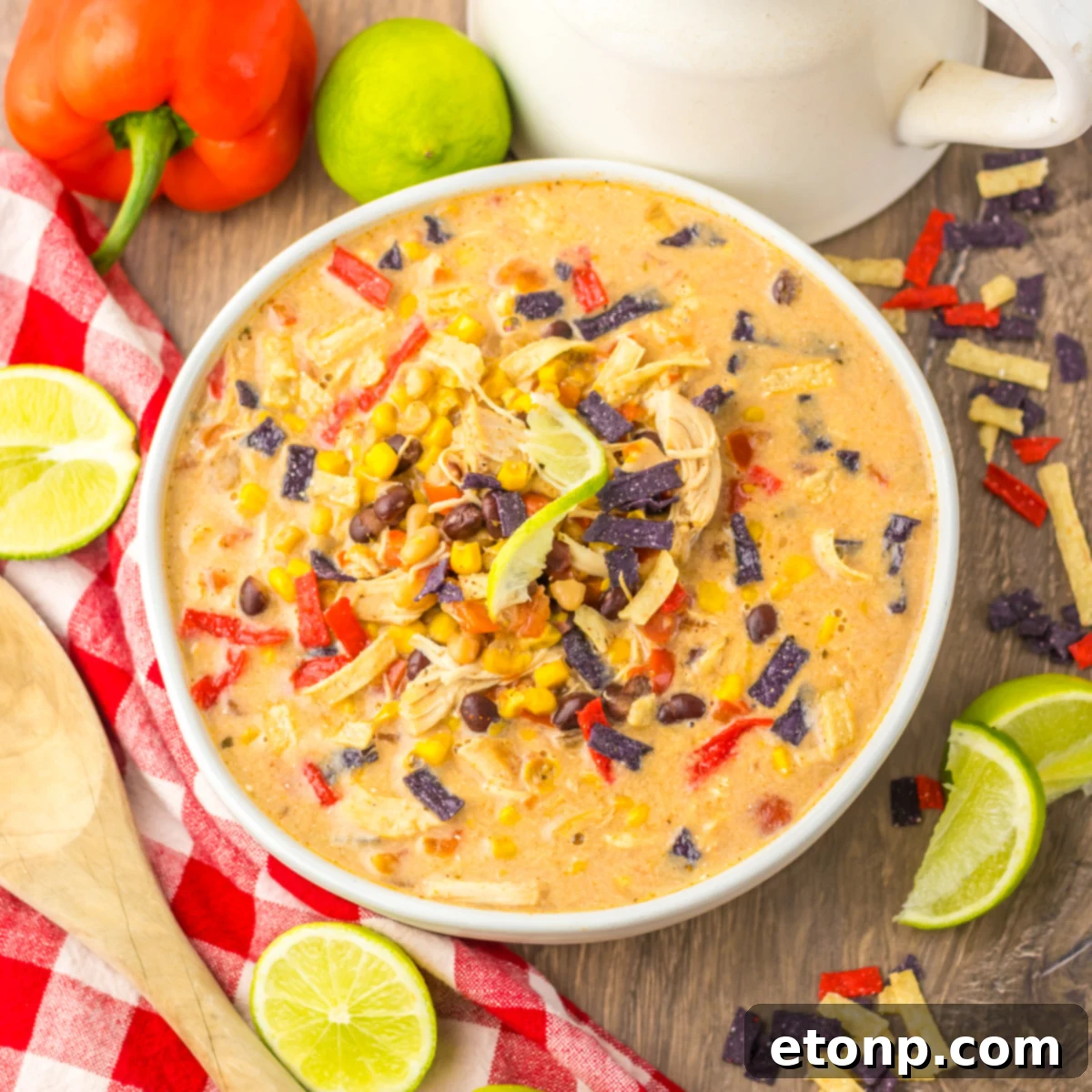 Overhead view of Tortilla Soup in a white bowl with a white and red checkered napkin and cut limes. 