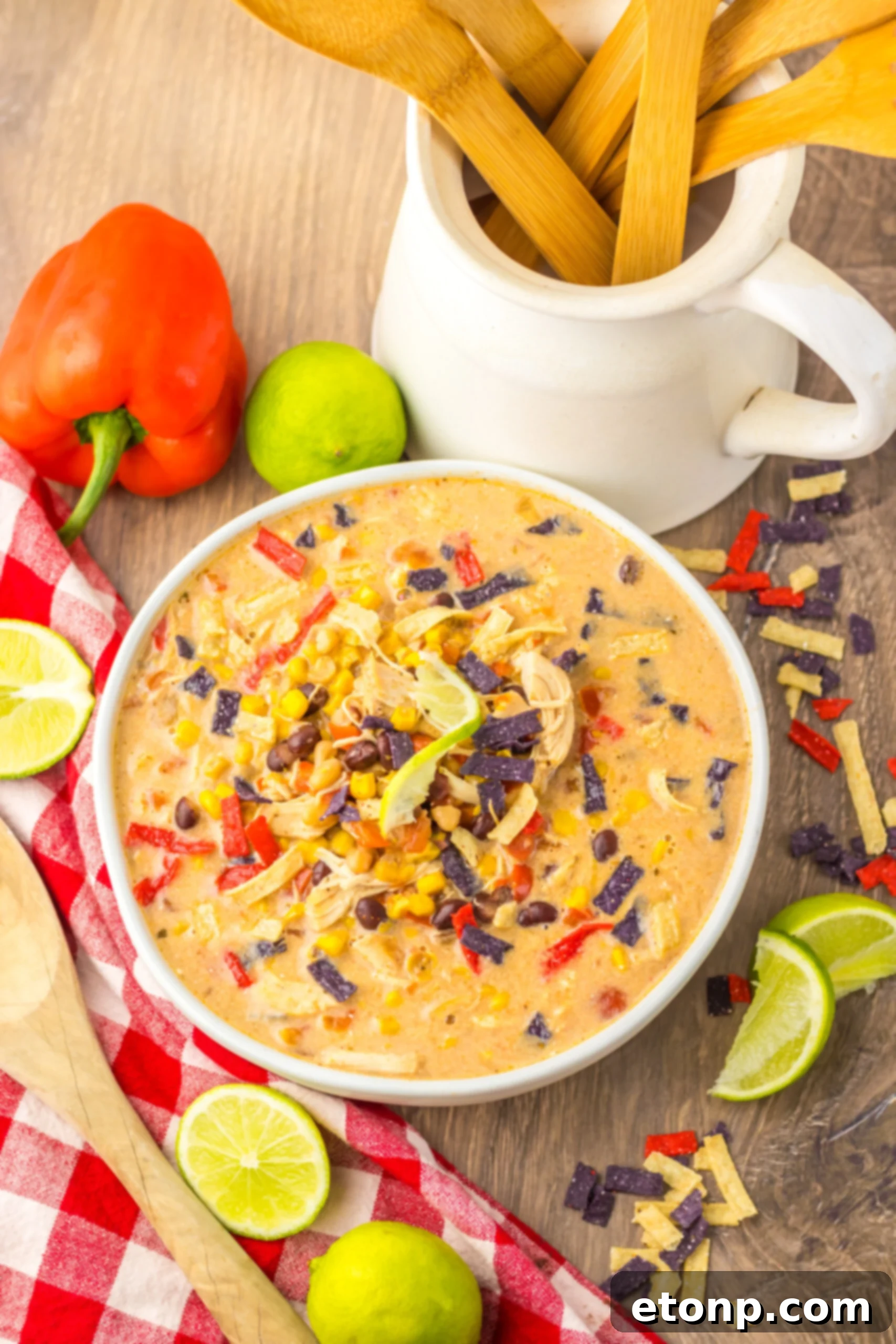 Close up side view of Slow Cooker Tortilla Soup in a white bowl with a tortilla chip topping and sliced limes. 