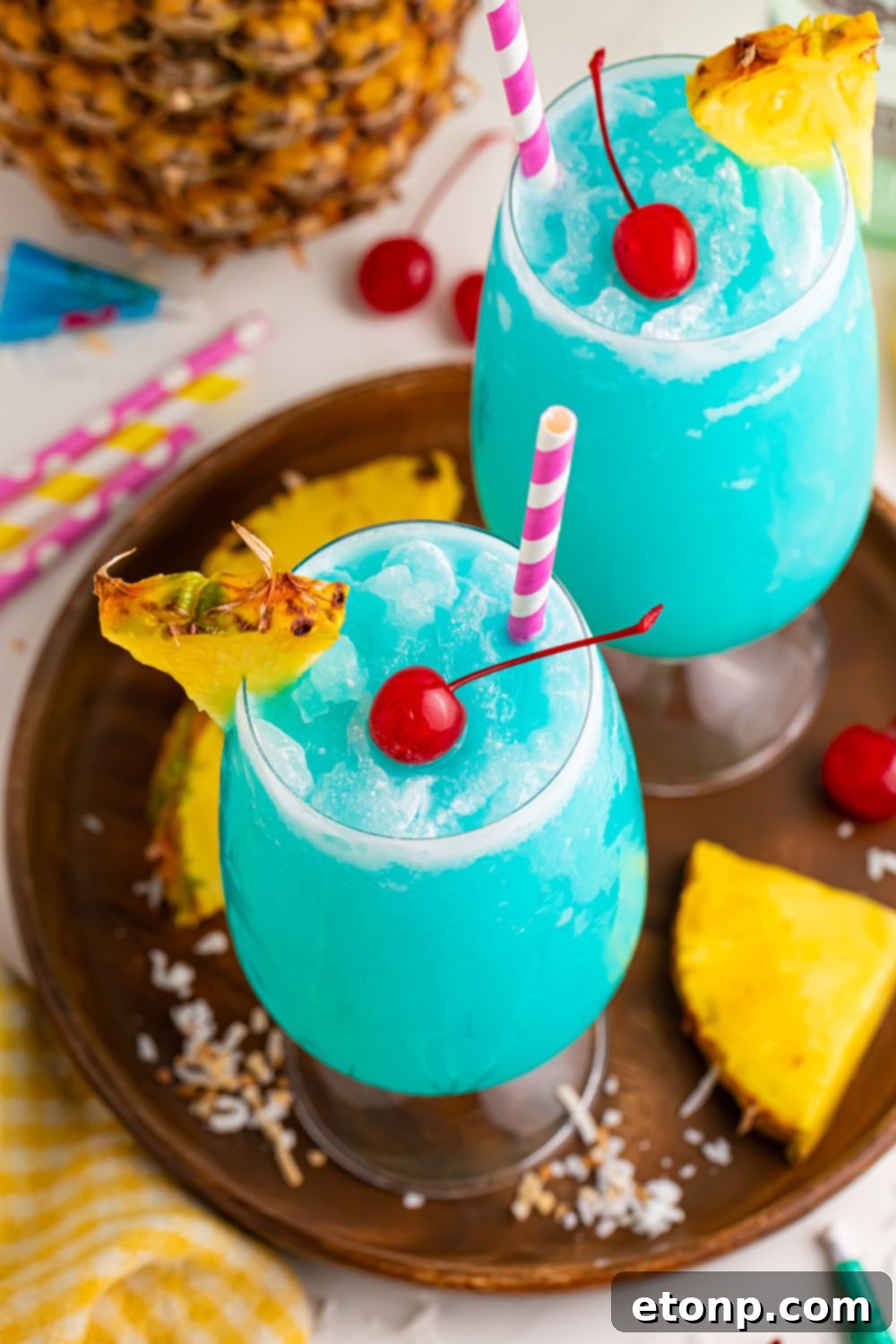Frozen Blue Hawaiian Cocktails with coconut and pineapple around the glasses and straws 