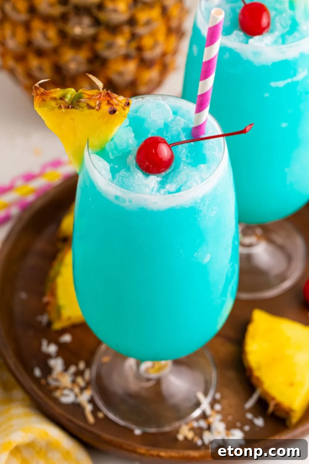 Frozen Blue Hawaiian Cocktails on table with a close up of class to see the cherry in center of drink and pineapple wedge on side of glass 