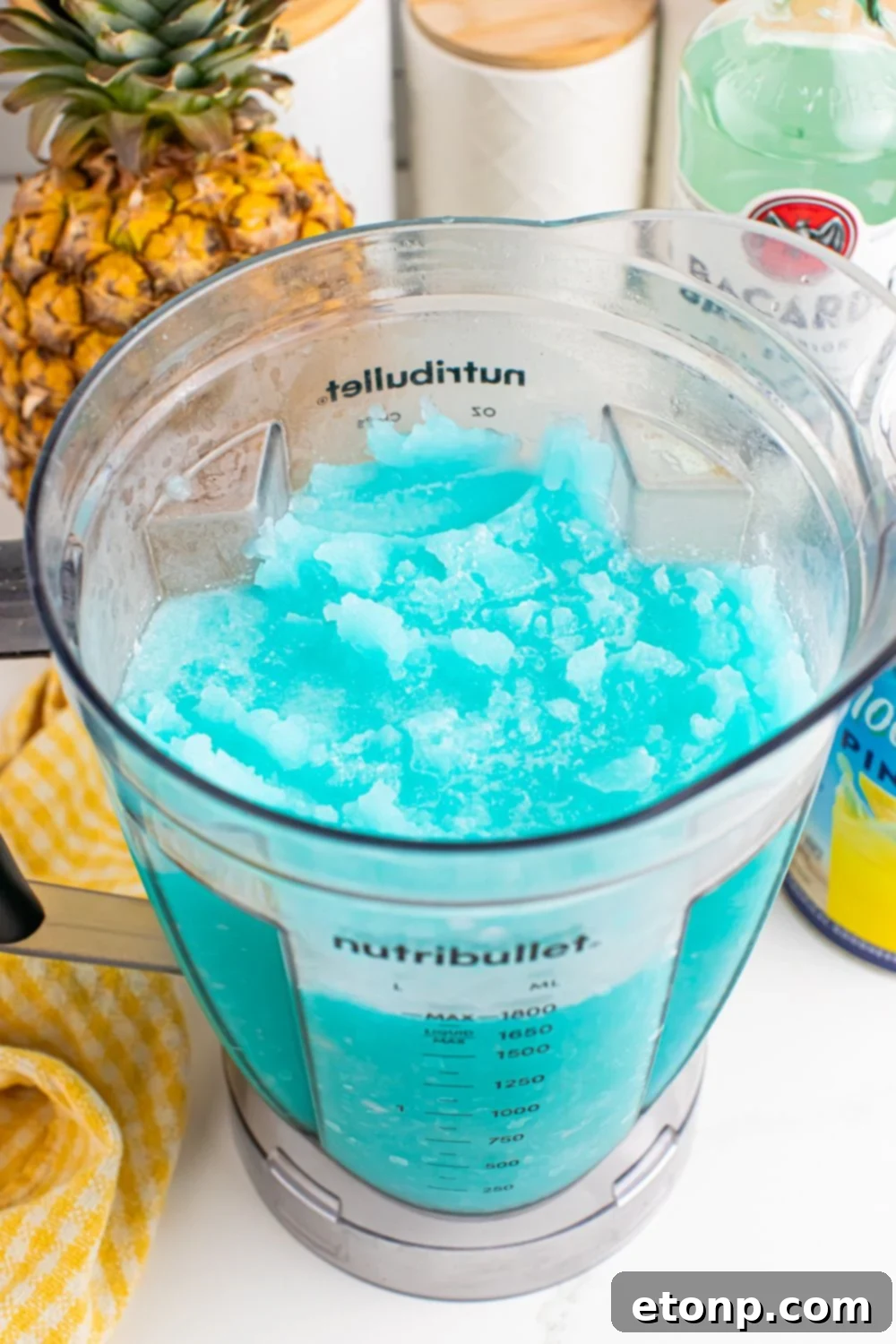 Frozen Blue Hawaiian Cocktail in a blender with ingredients for drink behind it on table 