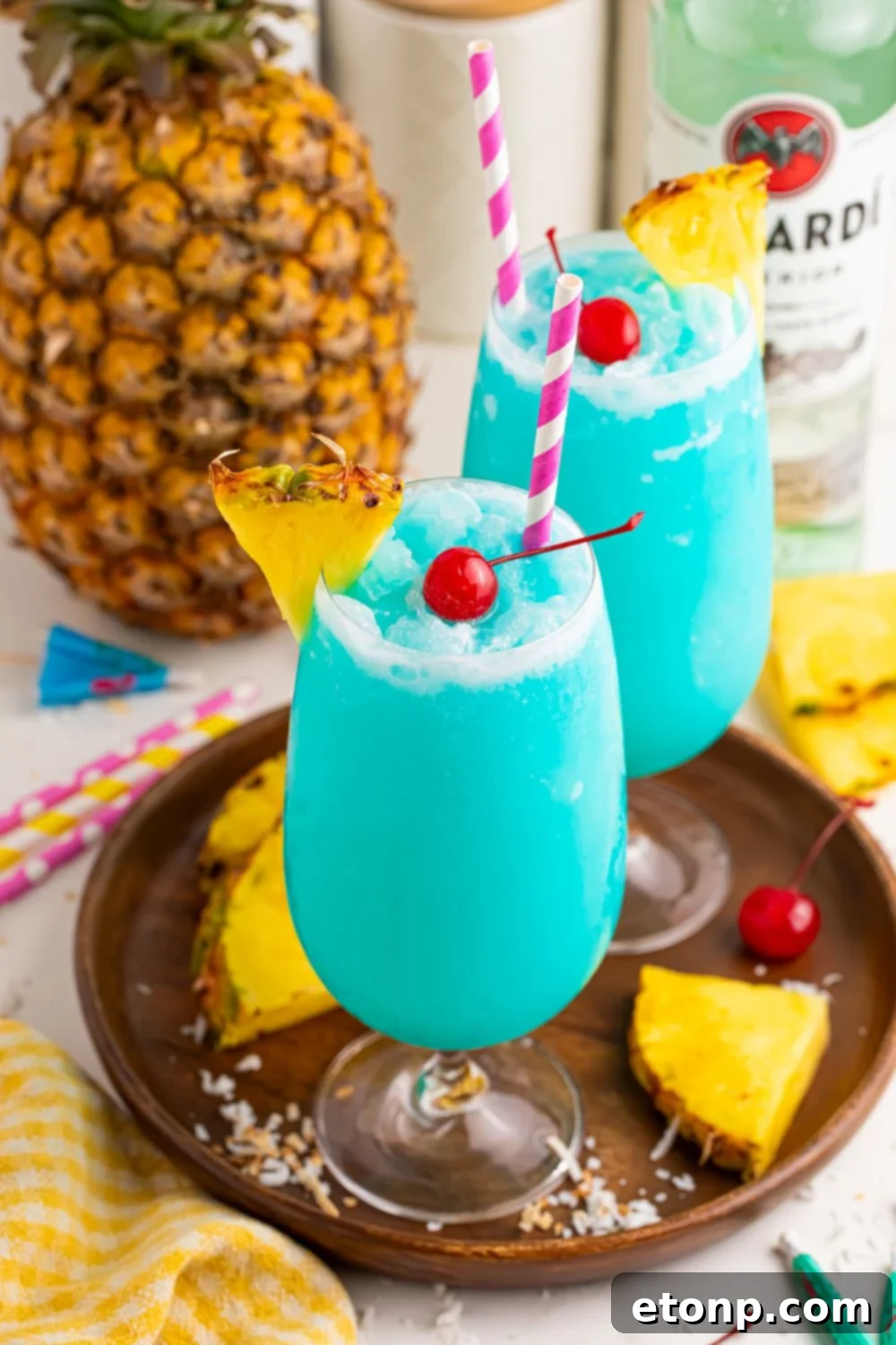 Frozen Blue Hawaiian Cocktails in glasses on table with a whole pineapple in background and sliced pineapple around table 