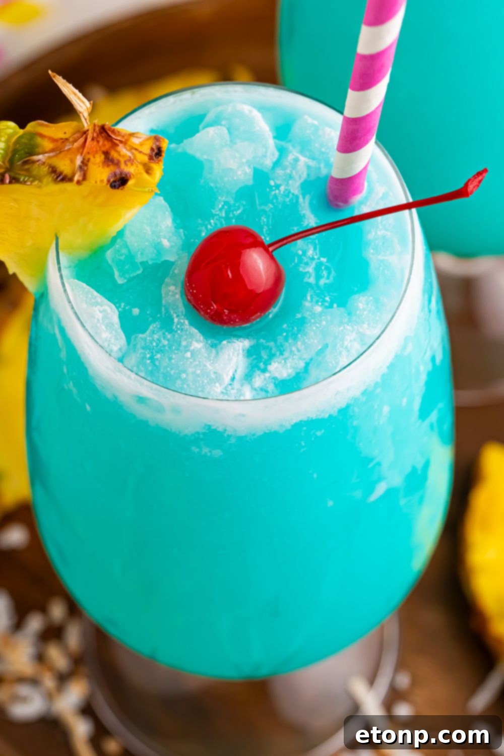 Frozen Blue Hawaiian Cocktail topped with a paper straw, cherries and pineapple 