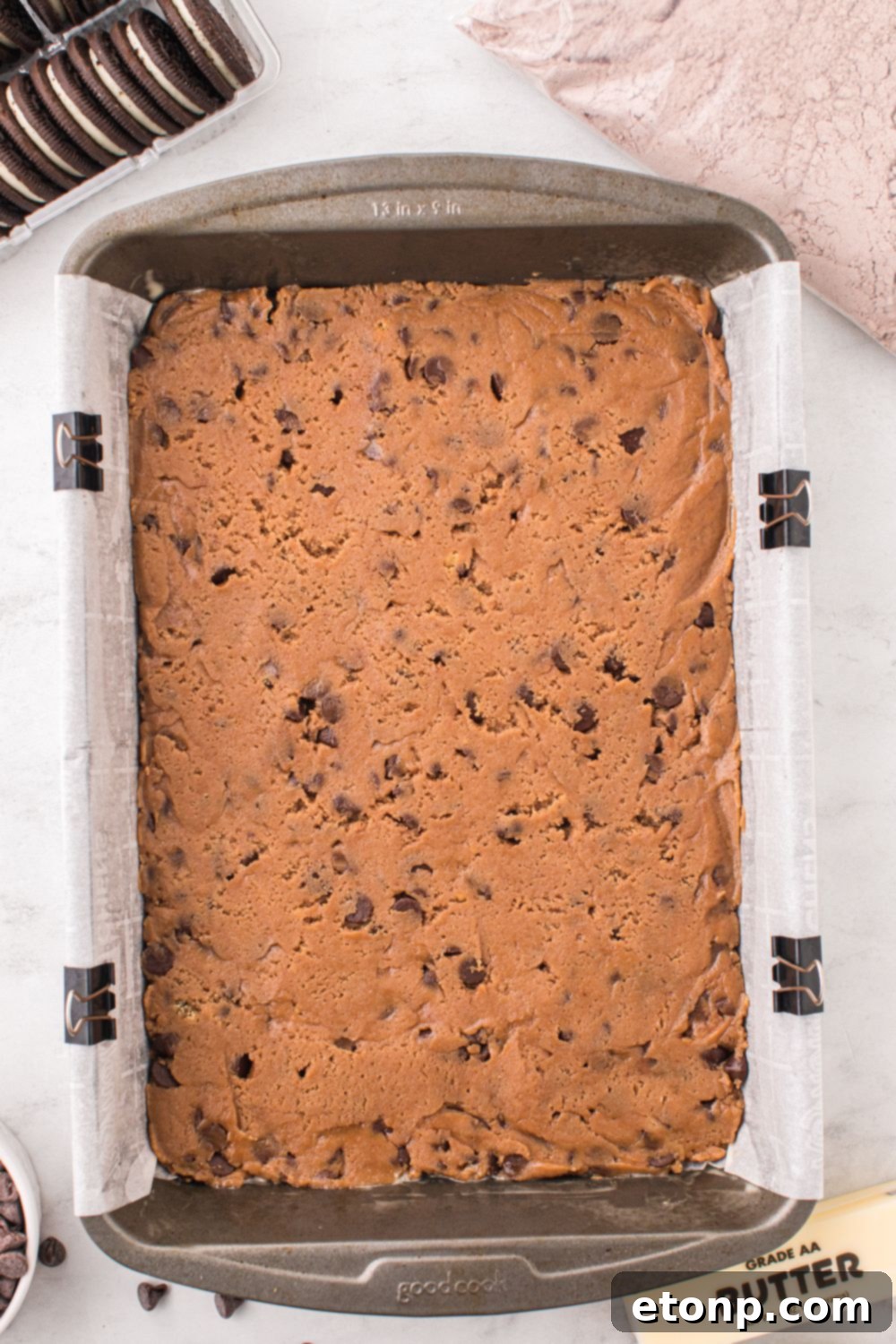 cookie dough batter in a 9x13 pan on table with Oreo cookies to side and a bag of brownie mix 