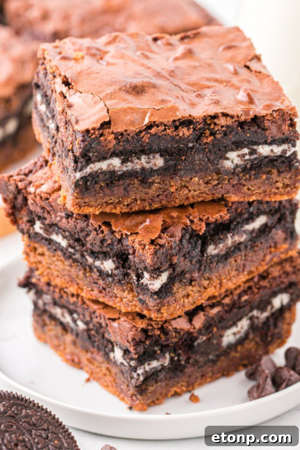 3 Slutty Brownies stacked on a plate with cookies and chocolate chips around the plate 