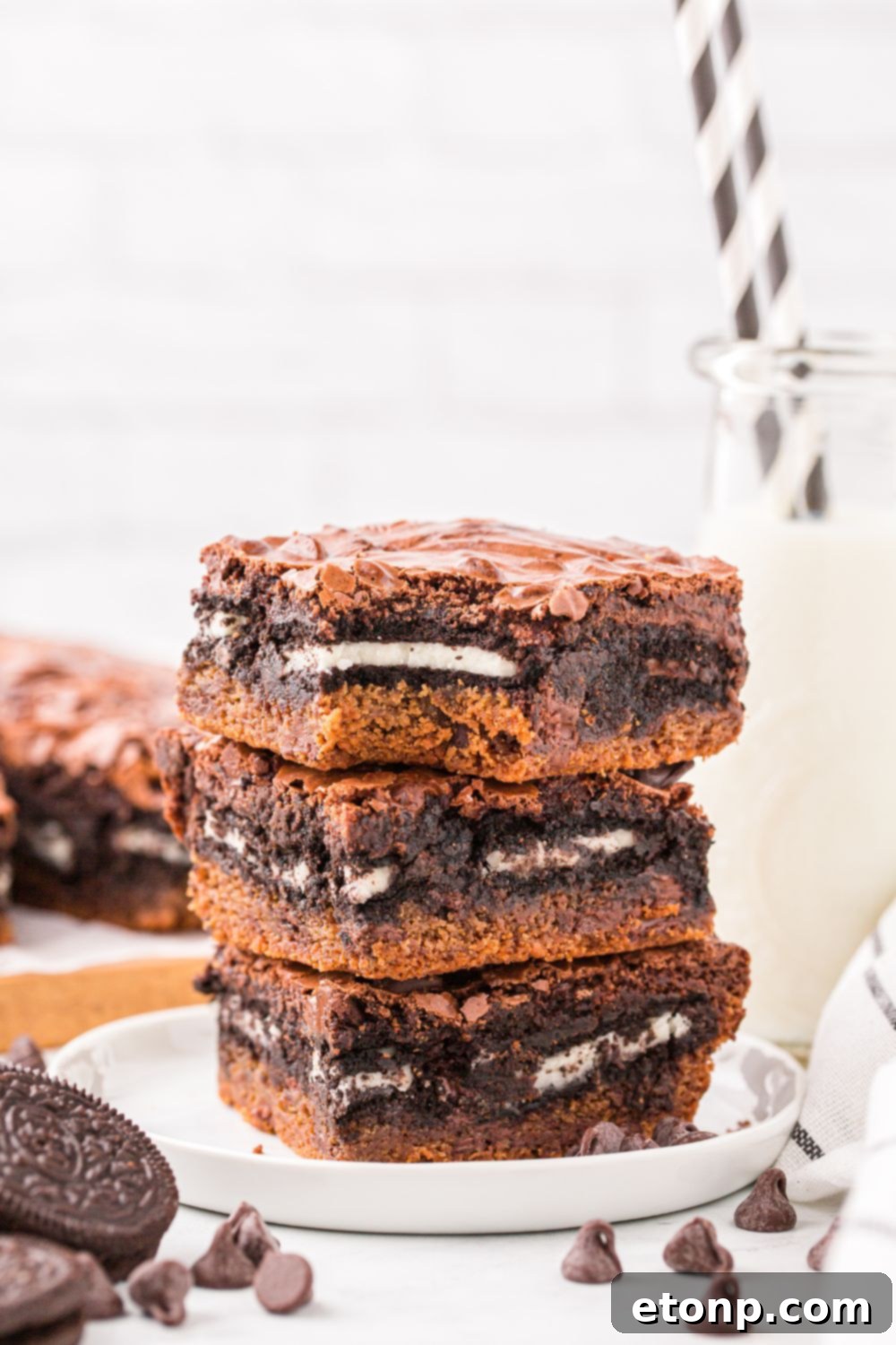 layered Slutty Brownies stacked on a plate with a glass of milk to side and more sliced bars on a tray