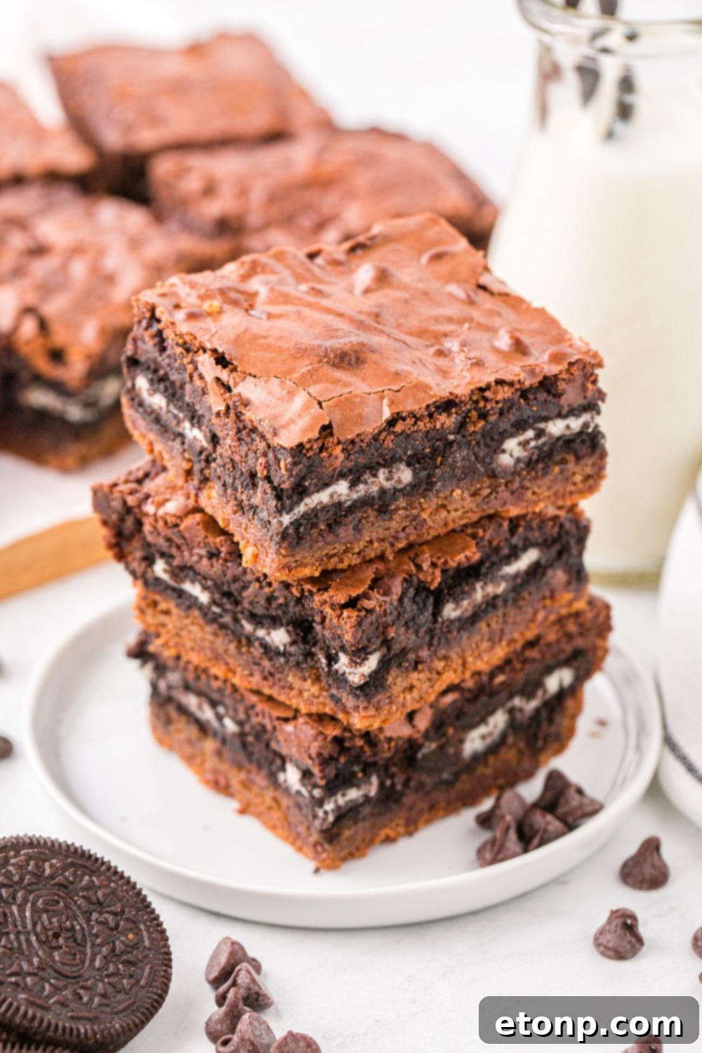Slutty Brownies stacked on a plate with chocolate chips and cookies on table around the bars 