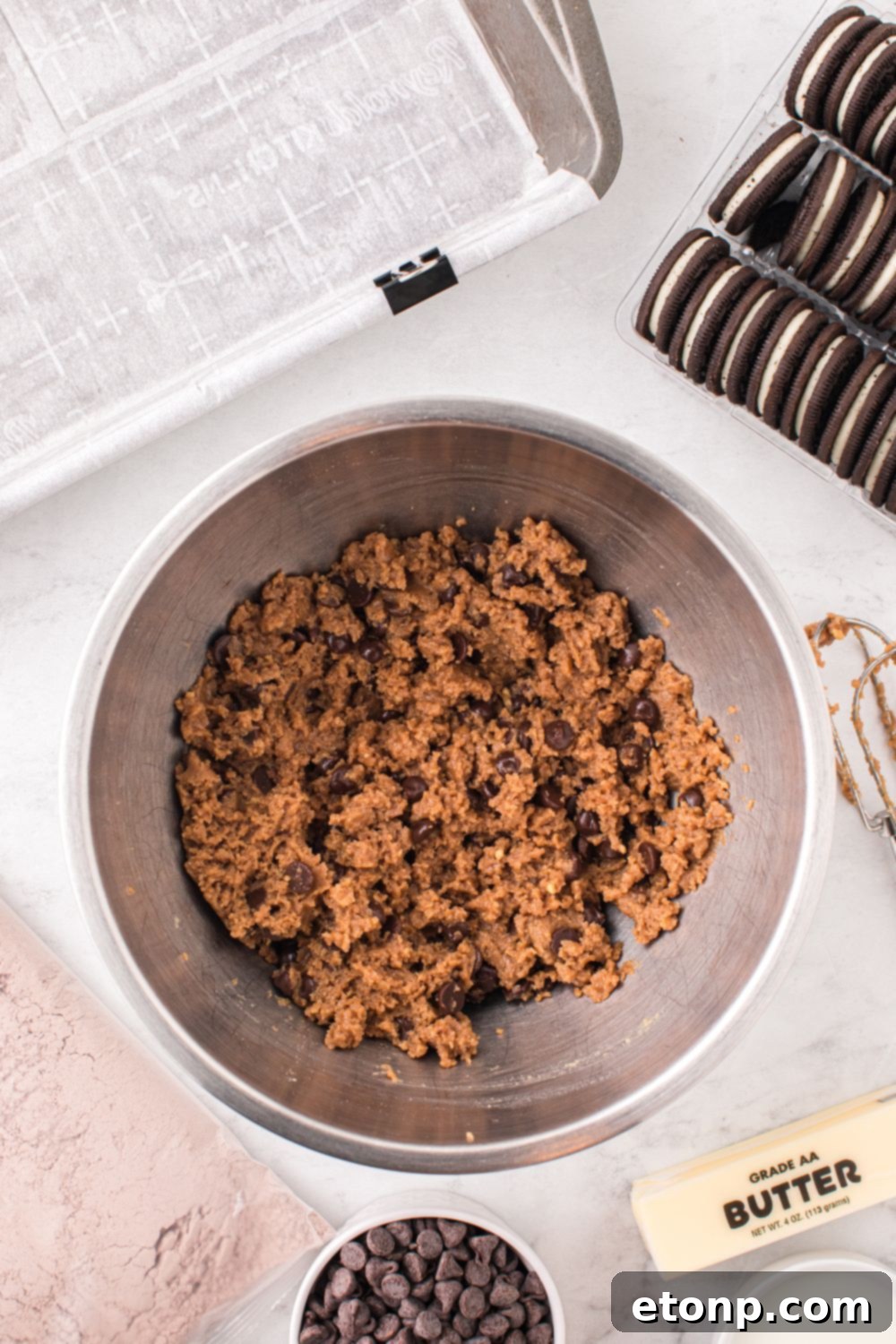 chocolate chip cookie dough in a bowl with a pan to side and cookies on other side of bowl