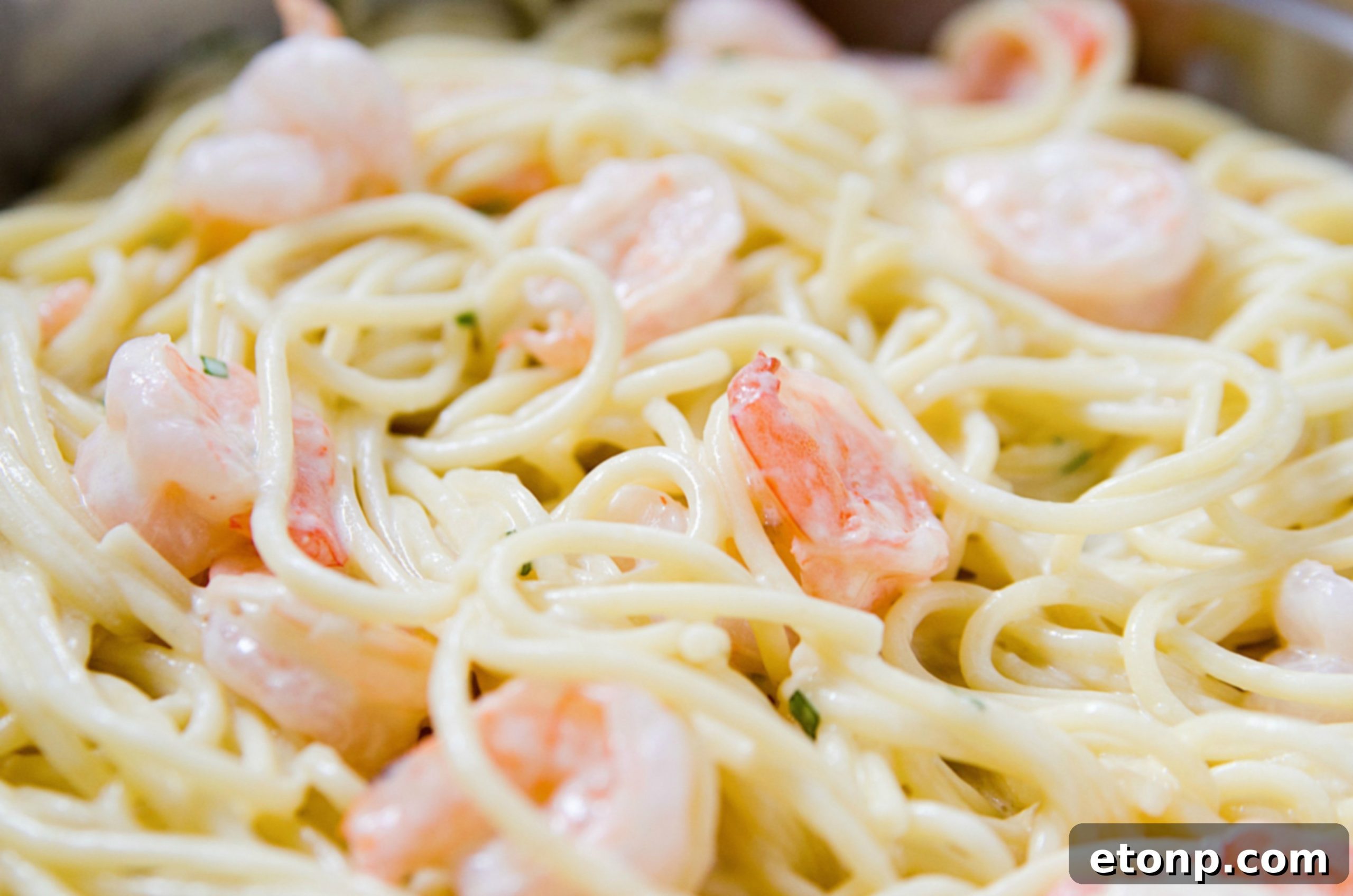 Cooked spaghetti being tossed into a skillet with the rich, creamy, and cheesy sauce, ensuring every strand is coated.