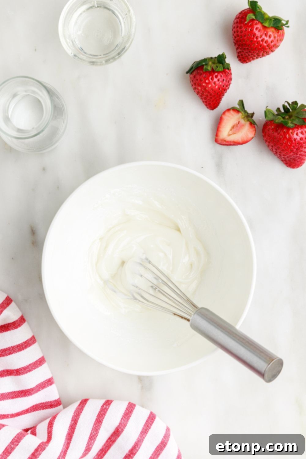 A smooth, white glaze meticulously prepared in a small white bowl, placed on a table, awaiting its use on the Deep Fried Strawberry Cheesecake Pies.