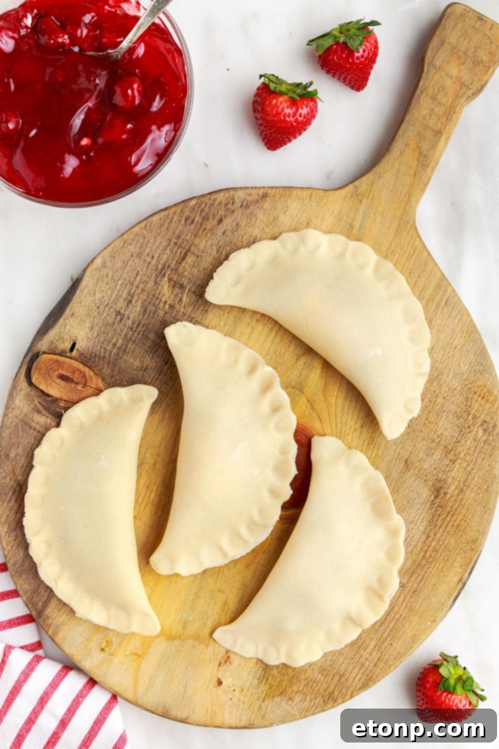 Neatly shaped hand pies arranged on a wooden tray, with a bowl of strawberry pie filling positioned to the side, showcasing preparation.