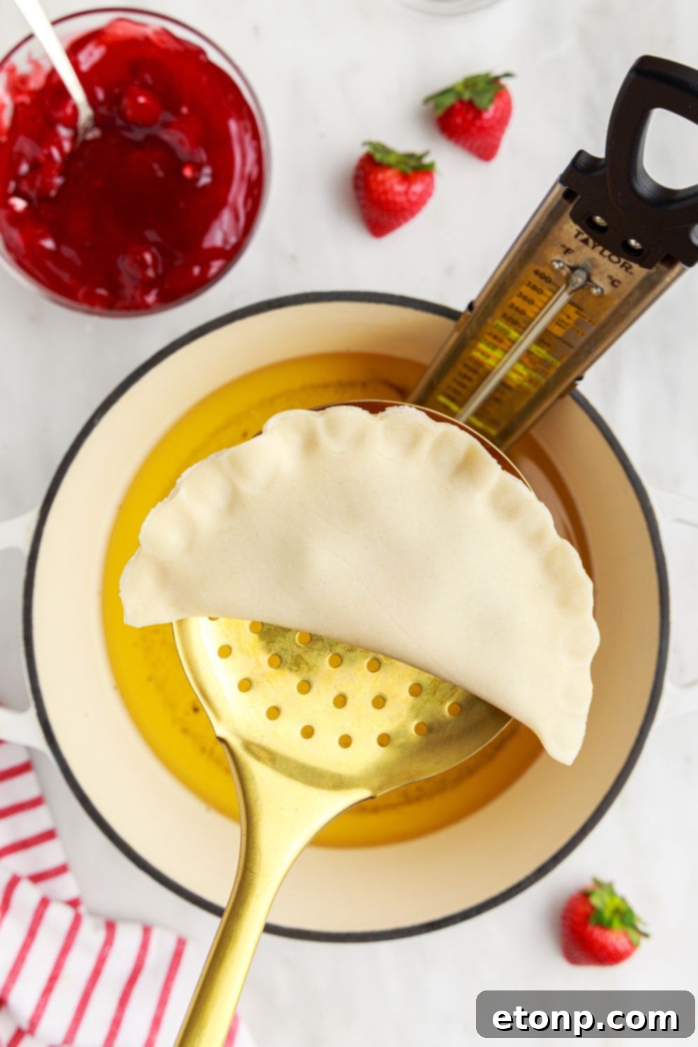 A raw Deep Fried Strawberry Cheesecake Pie gently held in a metal ladle, suspended just above a pot of hot frying oil, ready for cooking.