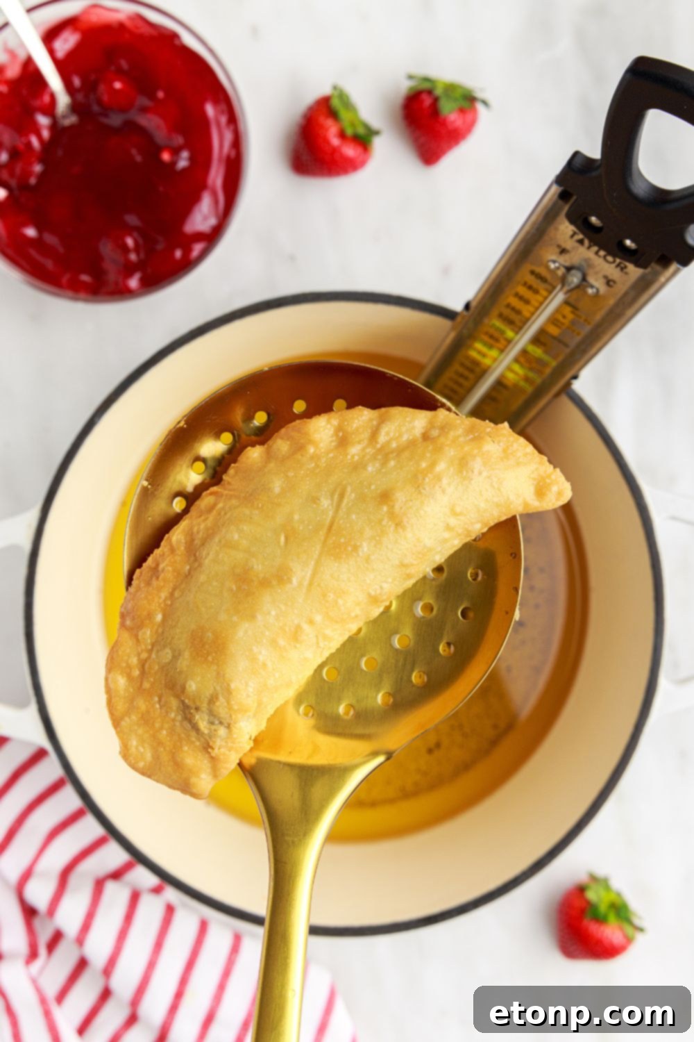A freshly fried Deep Fried Strawberry Cheesecake Pie delicately lifted from a pot of hot oil with a ladle, showing its golden-brown crust.