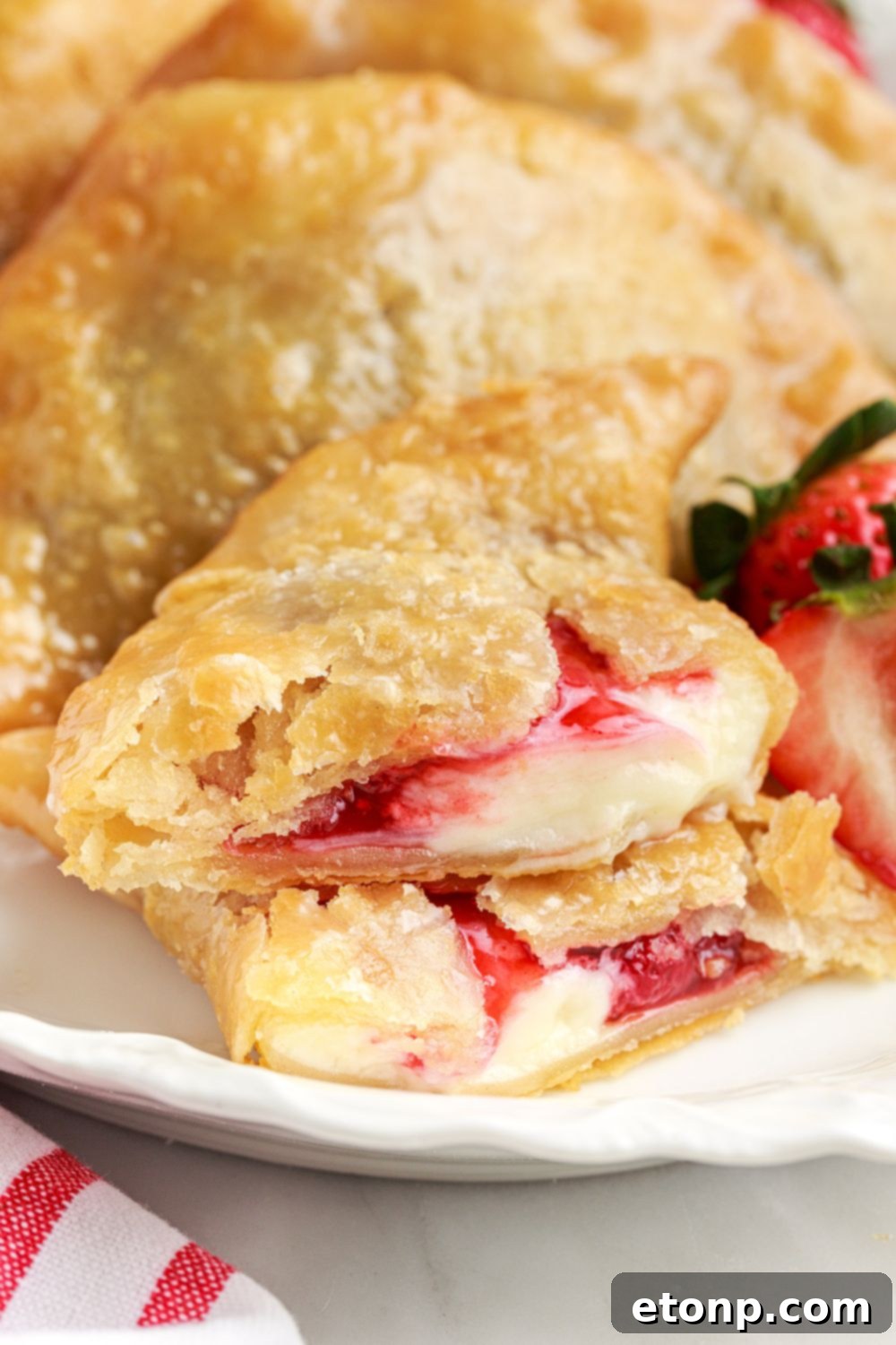 A platter of Deep Fried Strawberry Cheesecake Pies, with one pie meticulously cut in half to beautifully display the rich, creamy cheesecake and vibrant strawberry filling.