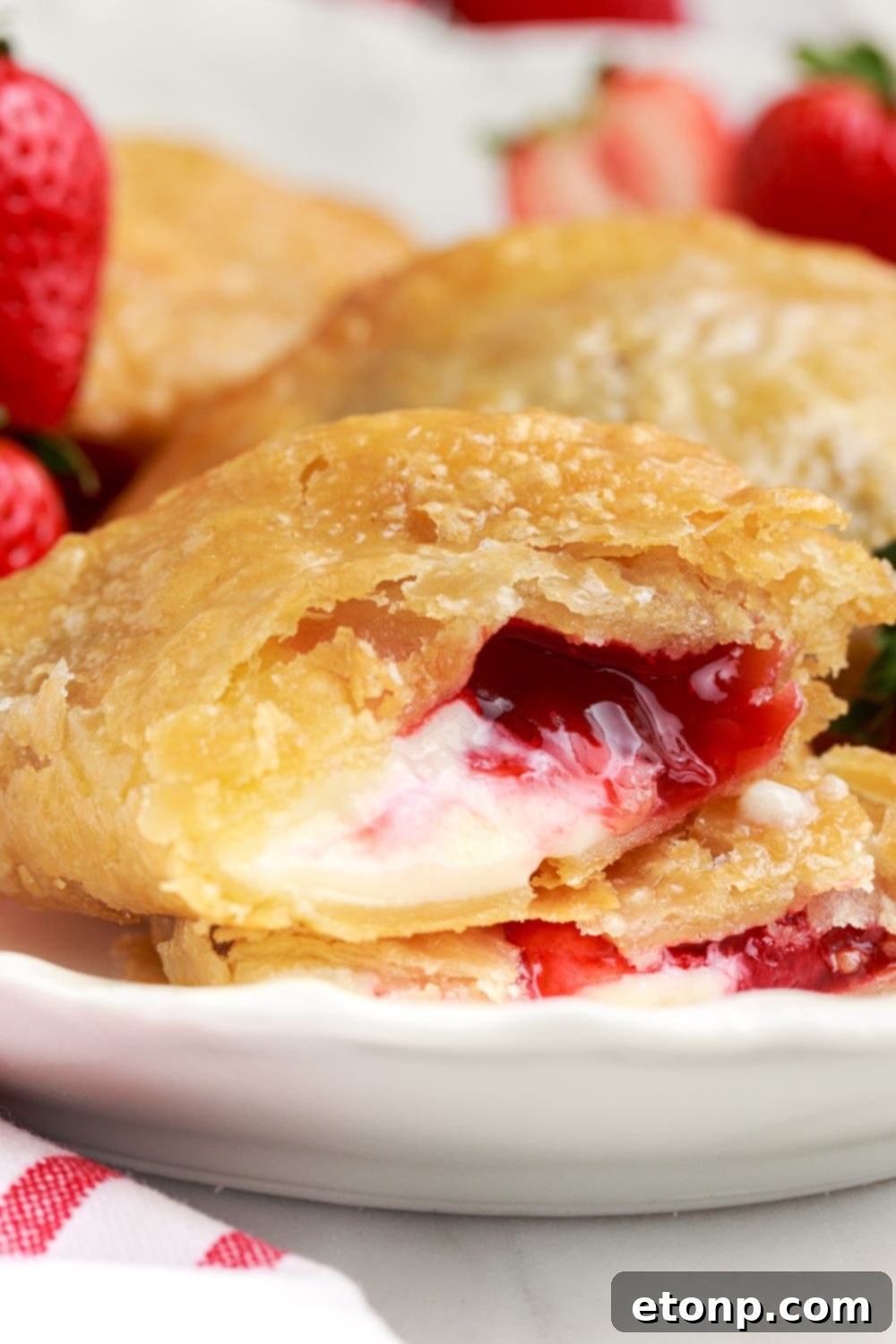 A Deep Fried Strawberry Cheesecake Pie resting on a table, with fresh strawberries and a red and white striped towel artfully placed to the side.