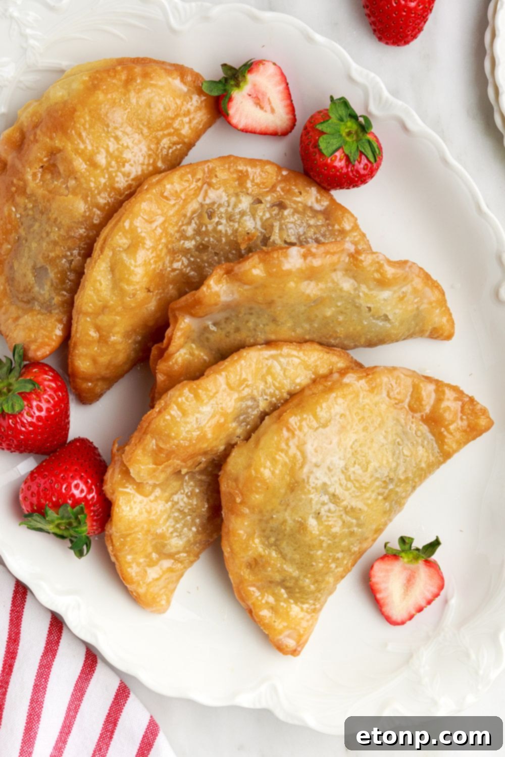 Deep Fried Strawberry Cheesecake Pies carefully placed on a tray, with fresh berries scattered charmingly around the side.