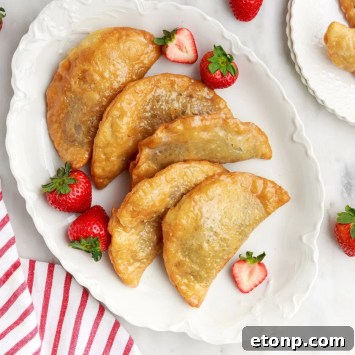 Deep Fried Strawberry Cheesecake Pies arranged on a rustic wooden tray on a table, with fresh strawberries scattered nearby.