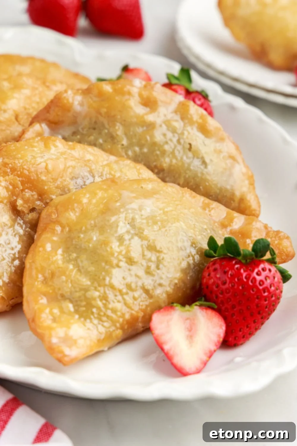 Deep Fried Strawberry Cheesecake Pies elegantly arranged on a platter, with some fresh strawberries thoughtfully placed on the plate as garnish.