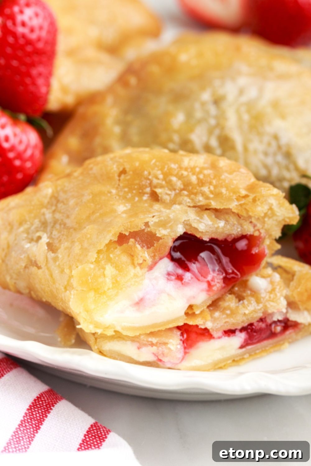 A Deep Fried Strawberry Cheesecake Pie, expertly cut in half and displayed on a table to reveal its rich, creamy filling, with fresh strawberries arranged to the side.
