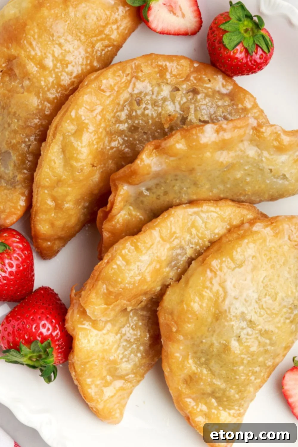 A single Deep Fried Strawberry Cheesecake Pie elegantly presented on a white plate, accompanied by a few fresh whole strawberries.
