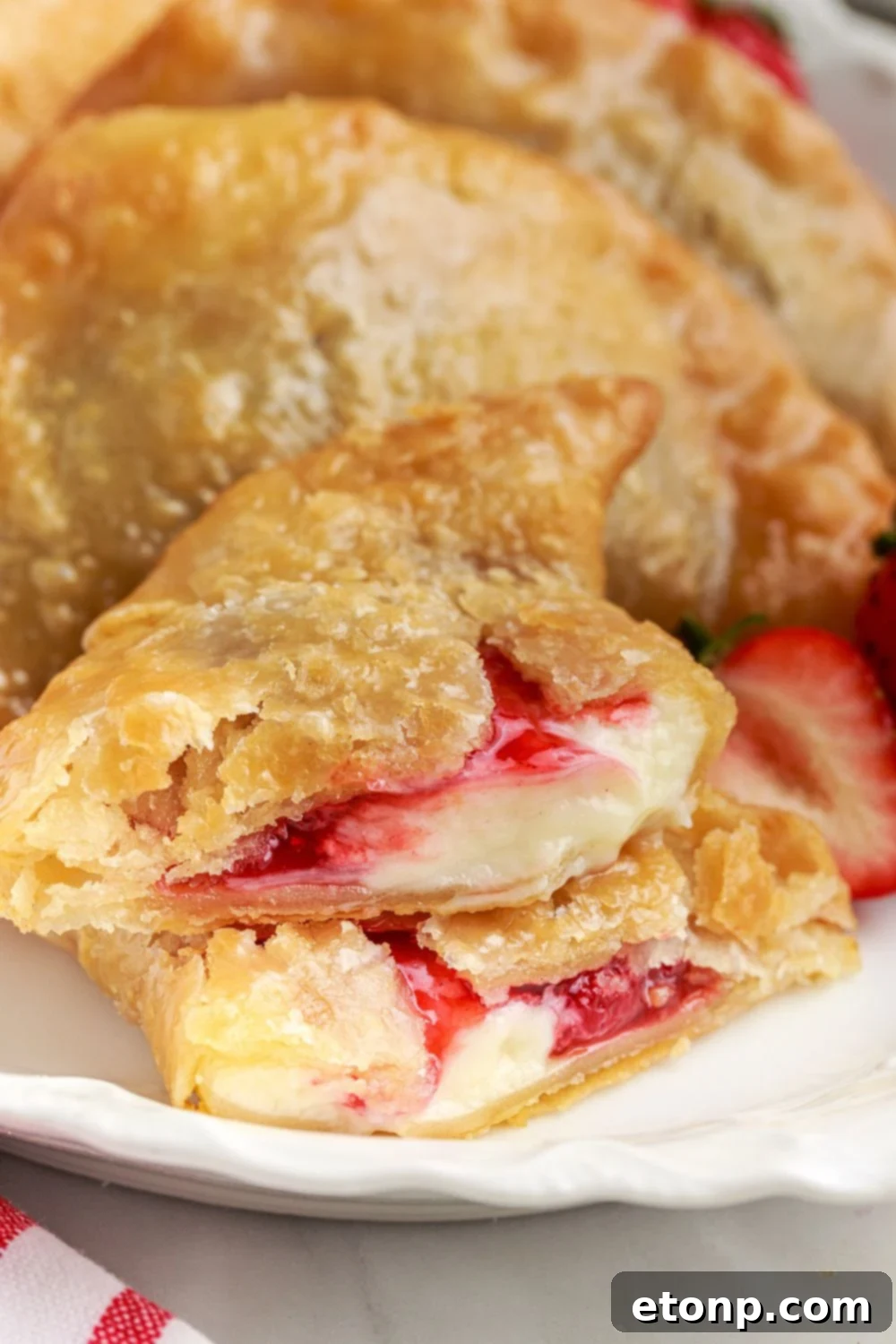 Deep Fried Strawberry Cheesecake Pies on a plate, with one pie expertly cut in half to showcase the rich, layered filling.