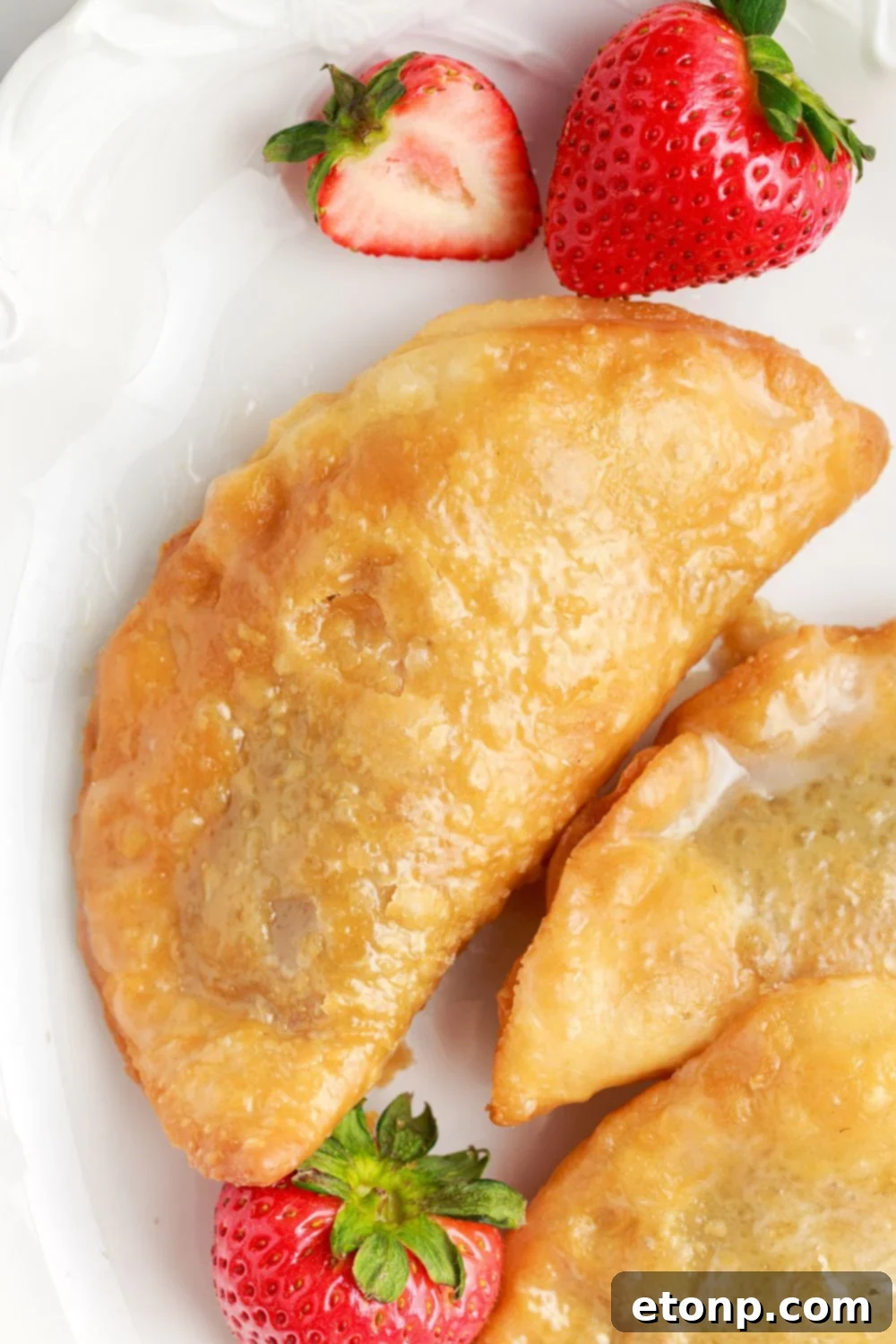 A single Deep Fried Strawberry Cheesecake Pie resting on a pristine white plate, with additional pies artfully scattered around the side.