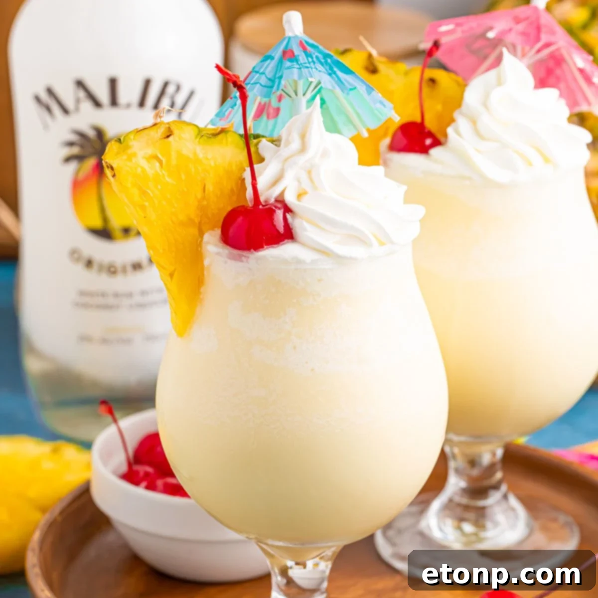 Frozen Malibu Piña Coladas in glasses with little umbrellas, pineapple slices and cherries