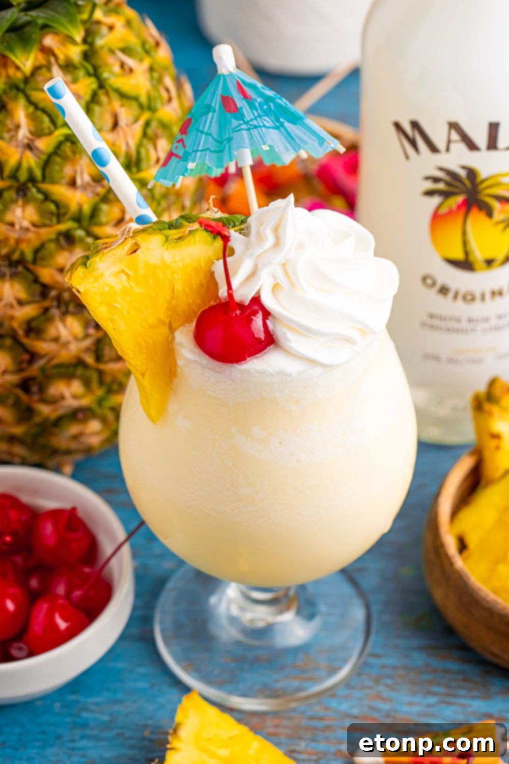 Frozen Malibu Piña Colada on table with whole pineapple and bottle of rum on table as well