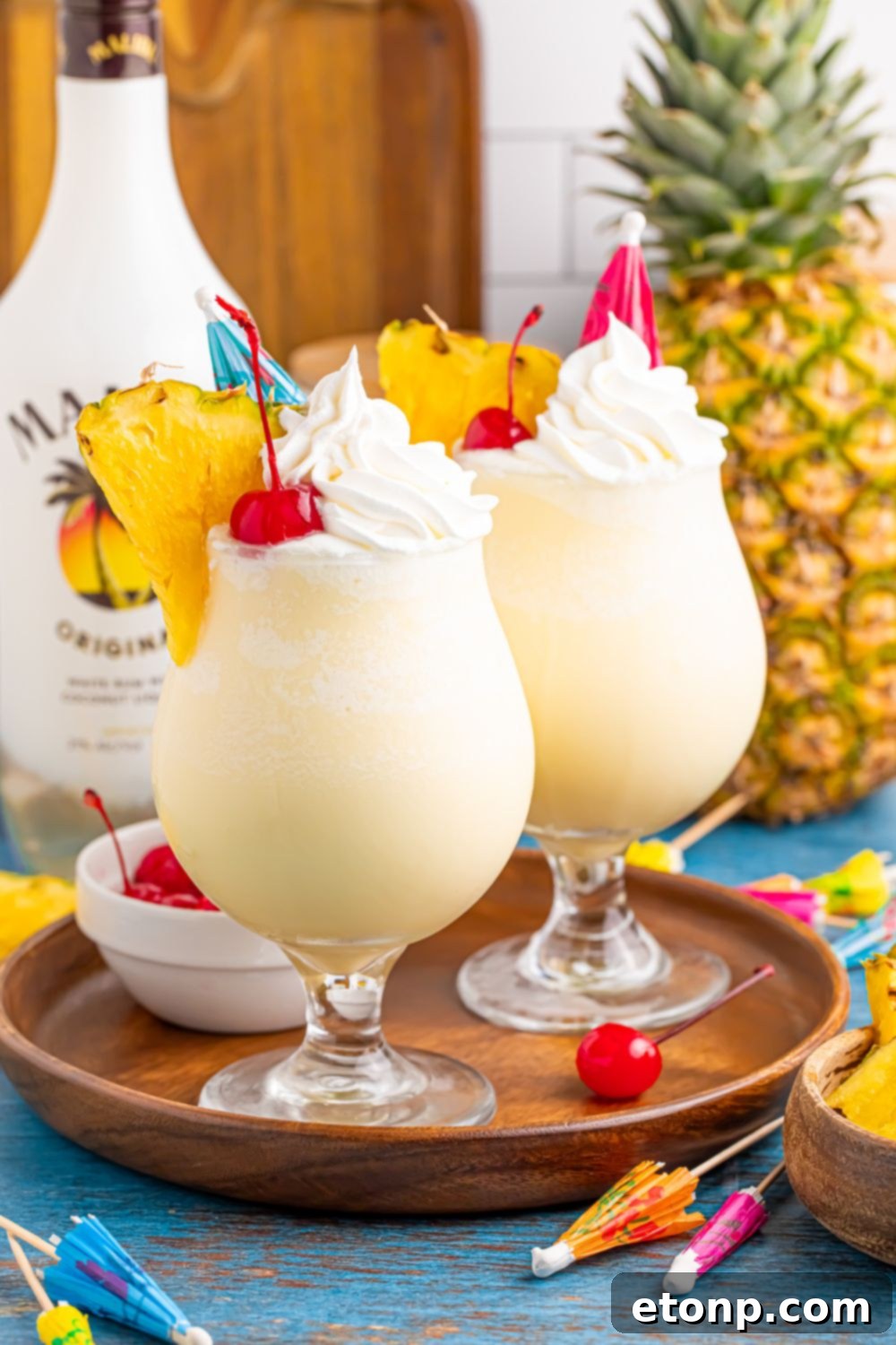 Frozen Malibu Piña Coladas on a tray with cherries and drink umbrellas scattered on table