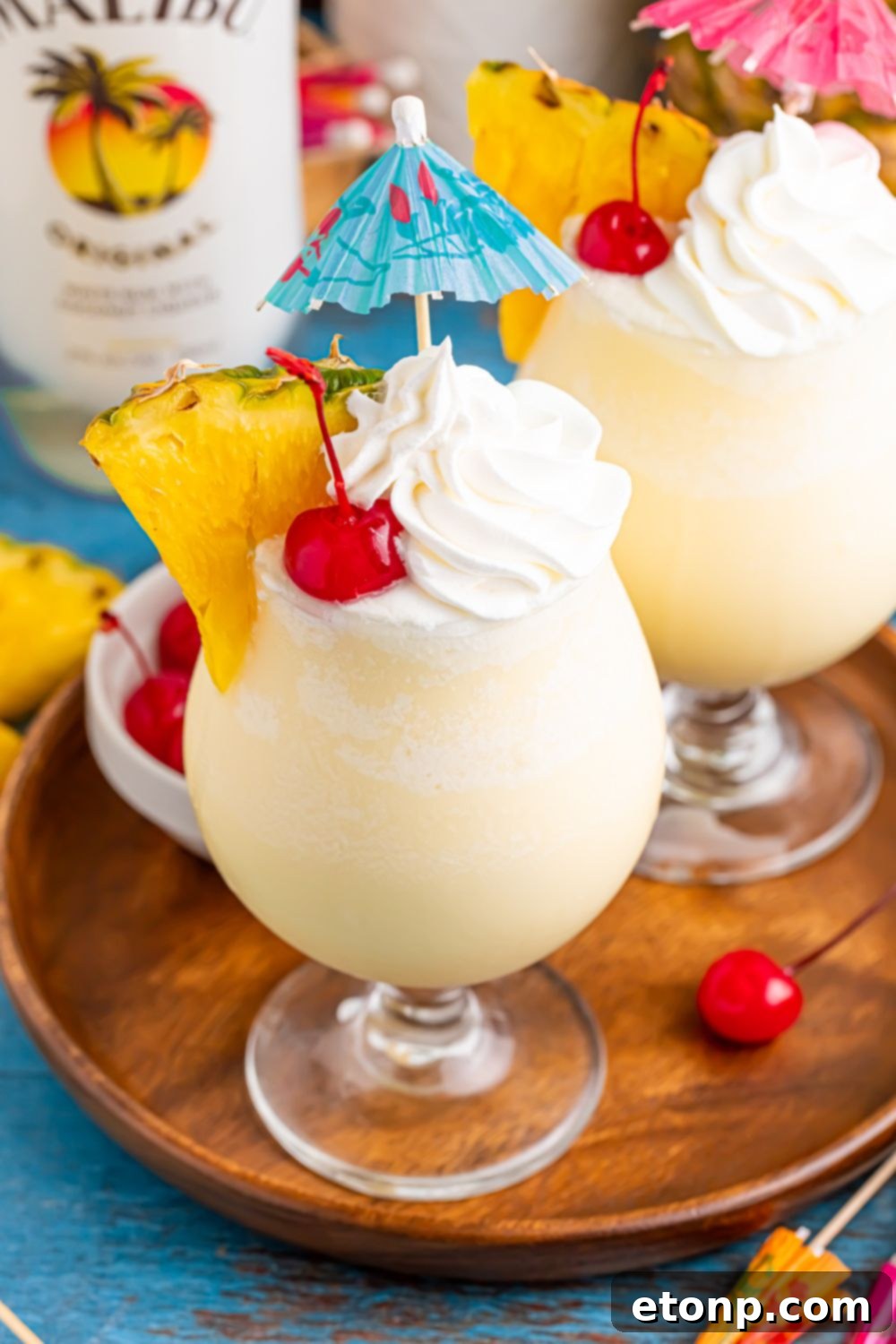 Frozen Malibu Piña Colada on table with pineapple wedges and whipped cream and umbrella topper