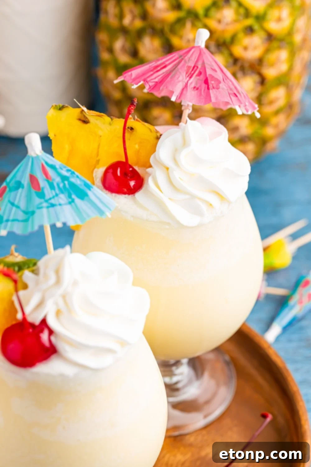 Frozen Malibu Piña Coladas on table with whipped cream, cherries, and umbrella, and more umbrella scattered on table