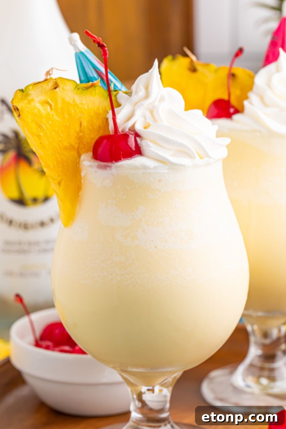 bottle of Frozen Malibu Piña Coladas sitting on a serving tray with rum and pineapple behind it on table