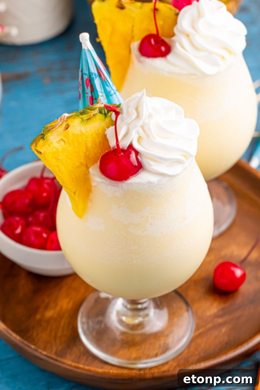 Frozen Malibu Piña Colada glasses on table with a small cocktail bowl of cherries to the side all on a tray