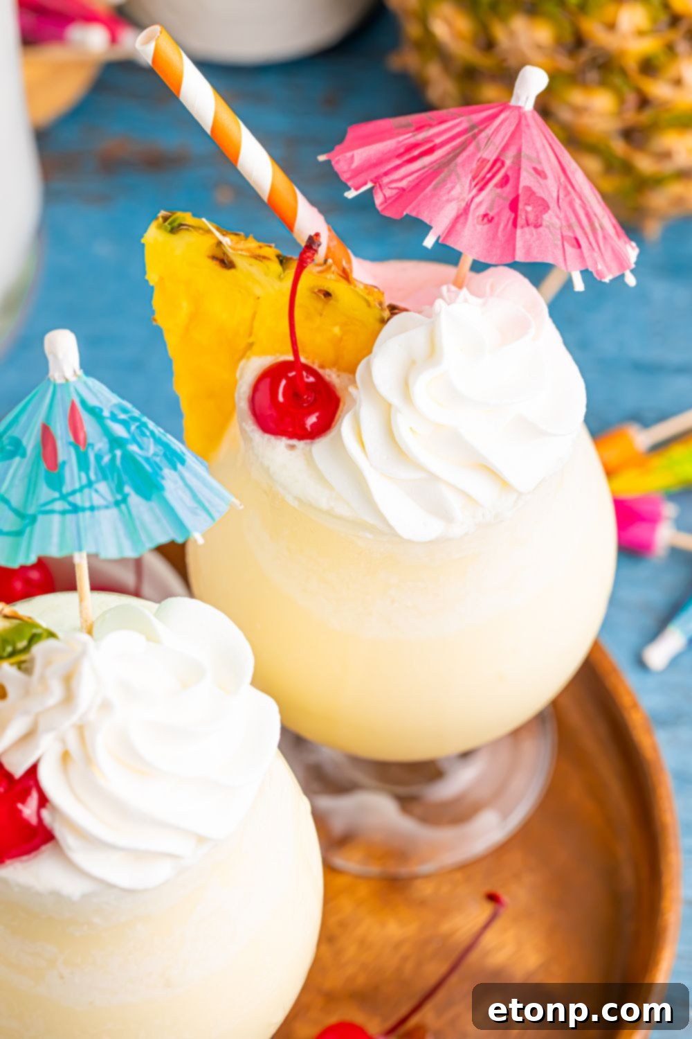 Frozen Malibu Piña Colada drinks on table with cherry, pineapple and umbrella in each glass on table