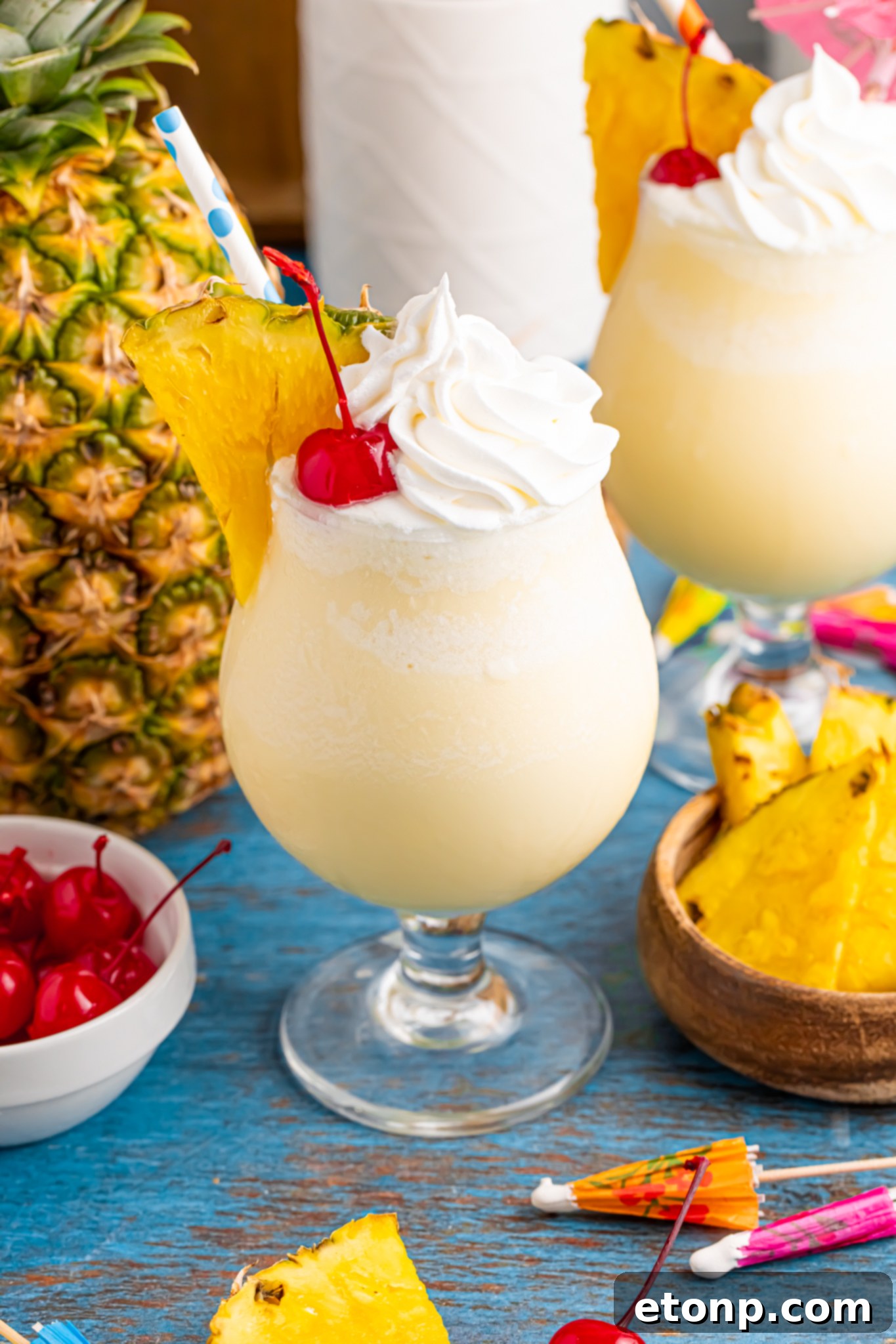 Frozen Malibu Piña Colada in a cocktail glass with a whole pineapple to side, bowl of cherries and pineapples