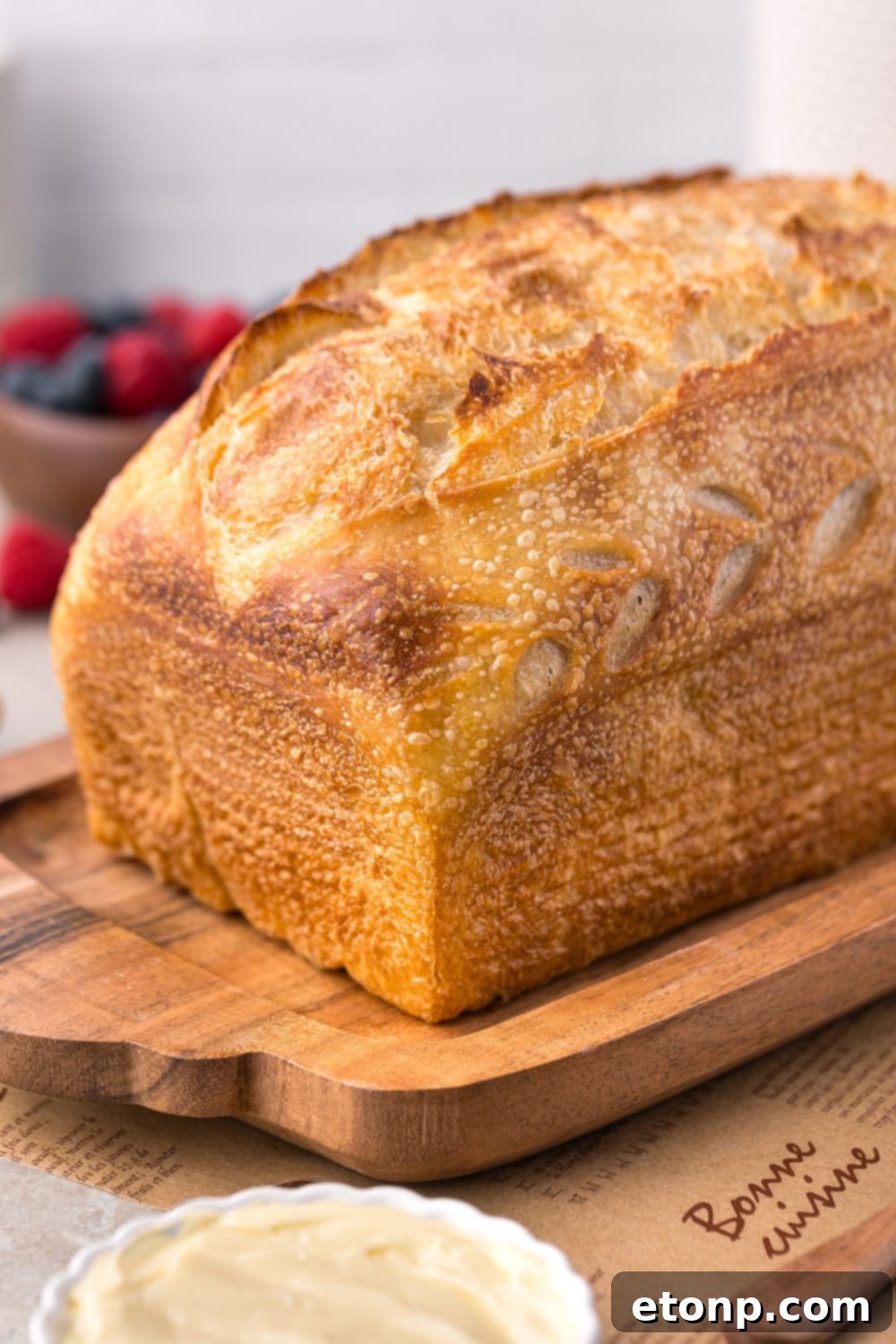 Homemade Sourdough Bread sitting on a cutting board with berries in a bowl to the side of table 