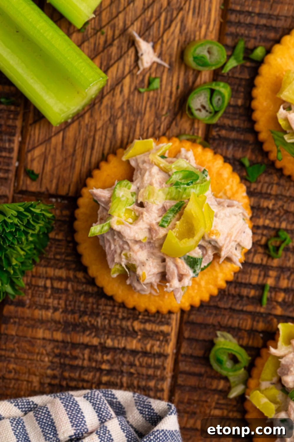 Looking down at a table to see celery, fresh herbs, and crackers with Pepperoncini Ranch Tuna Salad piled on top