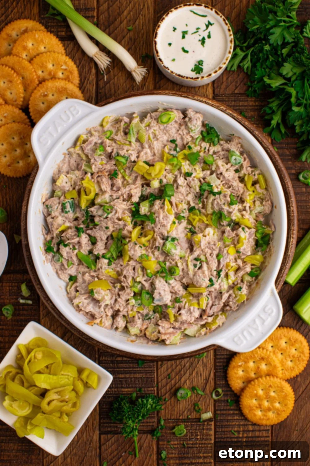 Pepperoncini Ranch Tuna Salad in a bowl with peppers, crackers, and fresh celery scattered on a table