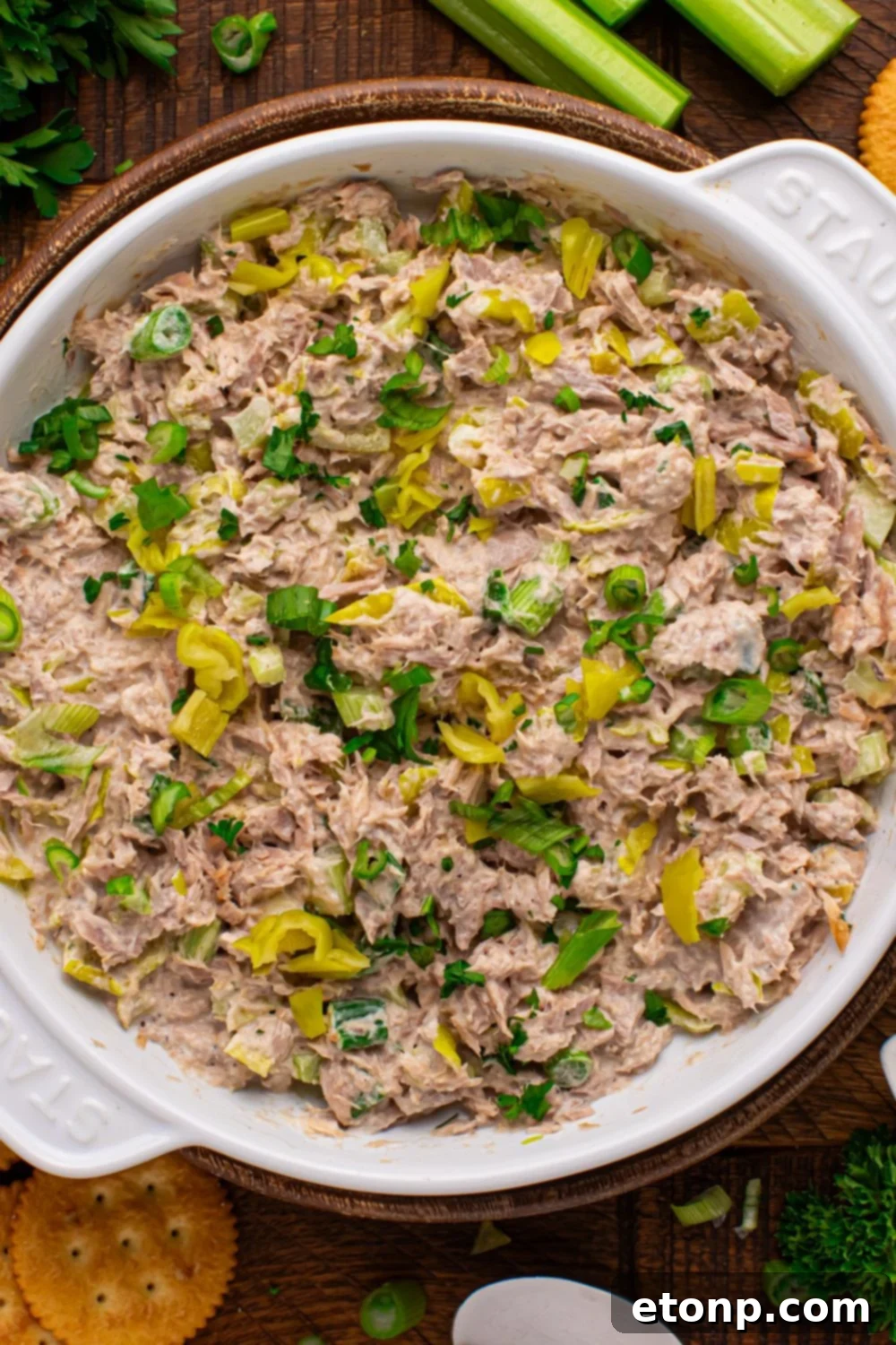 Overhead view of a large bowl of Pepperoncini Ranch Tuna Salad on a table, with celery and a fresh parsley bundle on the side