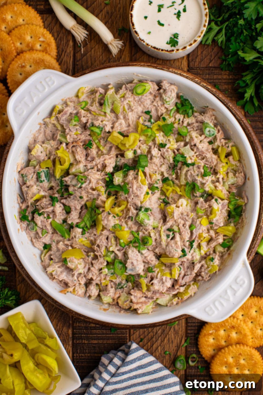 Overhead view of a white bowl filled with Pepperoncini Ranch Tuna Salad, surrounded by crackers and whole pepperoncini peppers