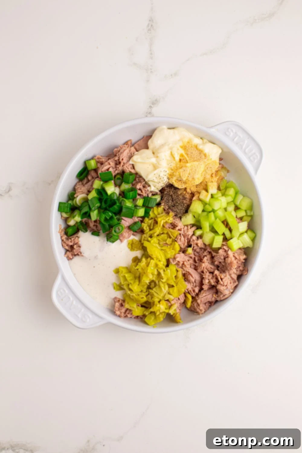 Pepperoncini Ranch Tuna Salad ingredients being added into a bowl on a white table