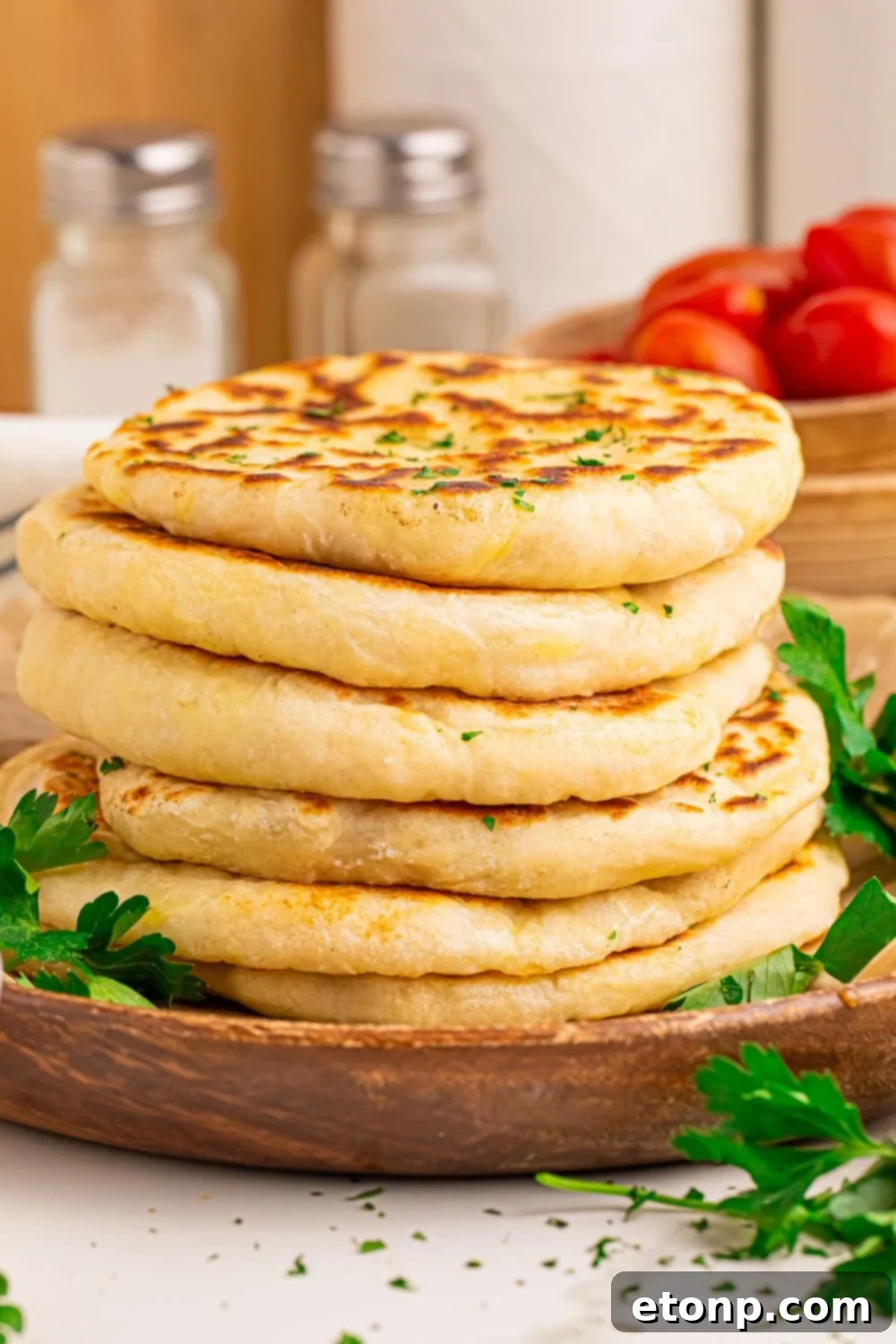3 Ingredient Flatbread stacked on top of one another with parsley on side and bowl of tomatoes behind it 