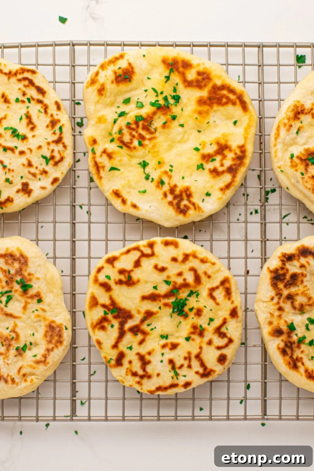 3 Ingredient Flatbreads spread out on cooling rack topped with butter and parsley flakes 